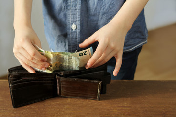 kid holds euro banknotes in his hand and puts them in a brown wallet, concept of pocket money, theft, shopping