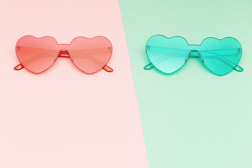 Minimal style fashion photography with heart shaped glasses on green and pink paper background. Modern sunglasses. Trendly summer concept. Copy space.