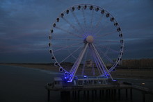 Giant Wheel Placed On A Pier Above The Ocean In The Night With A Blue Glare Over It