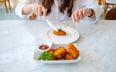 Wall Mural - Closeup image of a woman using knife and fork to eat fried chicken in restauran