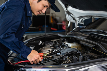 male mechanic charging battery car with electricity through jumper cables