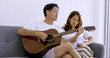 © ronnarong - Happy asian lover playing guitar and singing songs together in a room.