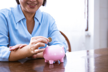 Wall Mural - Asain Elder  putting coin money to piggy bank saving, family, savings, age and people concept - smiling senior couple with money and piggy bank at home.