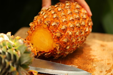 fresh ripe pineapple slicing girl hands on a wooden table in a tropical garden