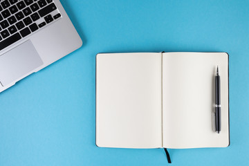 open diary or notebook with blank white pages and laptop computer on blue background template