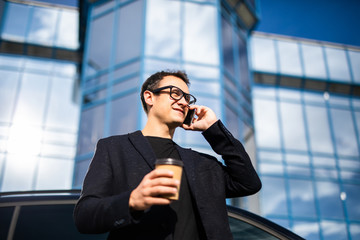 Wall Mural - Handsome professional fresh stylish modern business man calling on cellphone with coffee near skyscraper