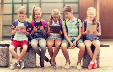 Sticker - primary education, friendship, childhood, technology and people concept - group of happy elementary school students with backpacks sitting on bench and talking outdoors