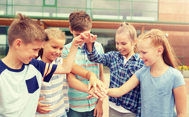 Wall Mural - primary education, friendship, childhood and people concept - group of happy elementary school students with hands on top outdoors