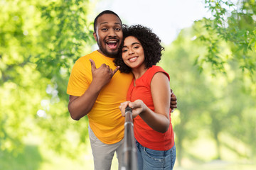 relationships and people concept - happy african american couple taking picture by selfie stick over green natural background