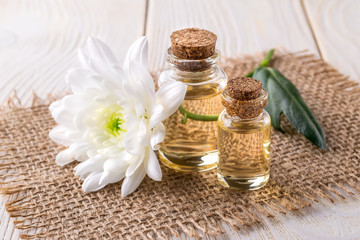 Two glass bottles of chrysanthemum essential oil and white chrysanthemum flower on a jute background. Spa, beauty, skincare and cosmetology concept.