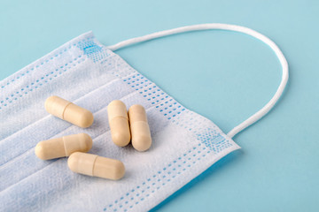 Pills or capsules on a disposable surgical mask over a blue background. Medical mask reduces the risk of infection. Airborne disease protection concept.