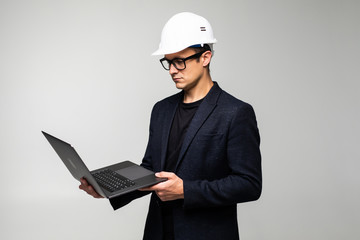 Wall Mural - Smart young architect wearing glasses and safety helmet which hands holding a laptop to check his planned work isolated on white background