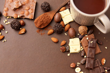 sweets, confectionery and food concept - hot chocolate with nuts, candies and cocoa powder on brown background