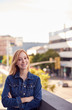 © Monkey Business - Portrait Of Smiling Young Businesswoman Standing Outside Office Building With City Skyline Behind