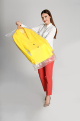 Sticker - Young woman holding hanger with jacket on light grey background. Dry-cleaning service