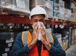 © StratfordProductions - Young african manager coughing and feeling sick while covering mouth with handkerchief in warehouse