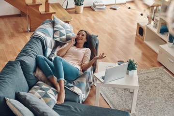 Wall Mural - Top view of beautiful young woman in casual clothing talking on the phone and smiling while spending time at home