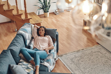 Wall Mural - Top view of relaxed young woman in casual clothing resting on sofa while spending time at home