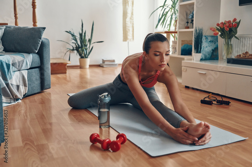 Cuadros en Lienzo Attractive young woman in sports clothing stretching on exercise mat while spend