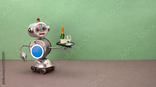 A four-wheeled robot waiter carries a tray with wine glasses and a bottle of champagne. Autonomous mechanical robotic restaurant service concept. Green wall, gray floor background. copy space.