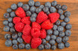 raspberry heart in blueberry heap on wood background