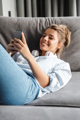 Sticker - Image of smiling nice woman using cellphone while lying on sofa