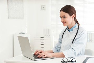 Wall Mural - Young female doctor working with laptop at table in office