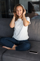 Canvas Print - Image of smiling woman using wireless headphones while sitting on sofa