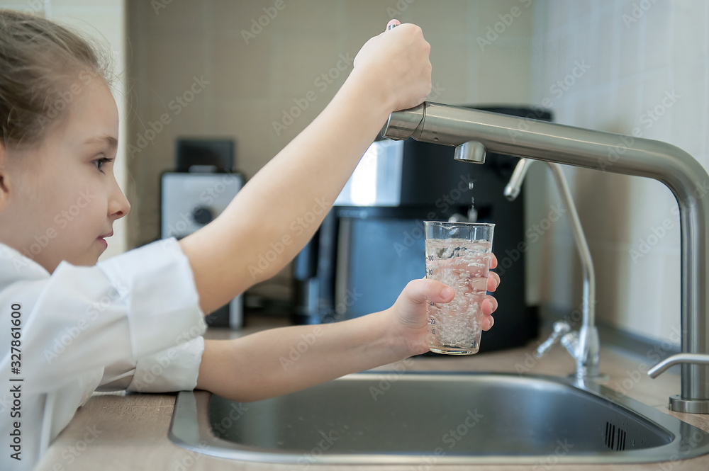 Little girl open a water tap with her hand holding a transparent glass. Kitchen faucet. Filling cup beverage. Pouring fresh drink. Hydration. Healthcare. Healthy lifestyle. World water day