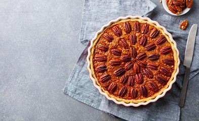 Pecan pie, tart in baking dish. Traditional festive Thanksgiving dessert. Grey background. Top view.