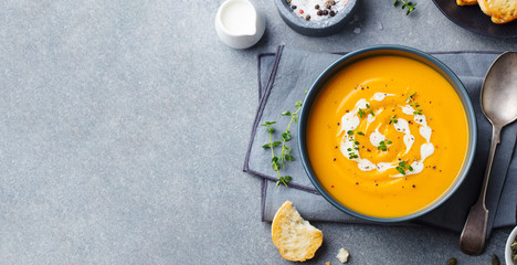 Wall Mural - Pumpkin, carrot cream soup in a bowl. Grey background. Top view. Copy space.