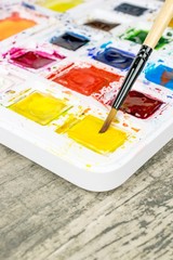 An artists paint brush and a box of messy colourful water colour paints