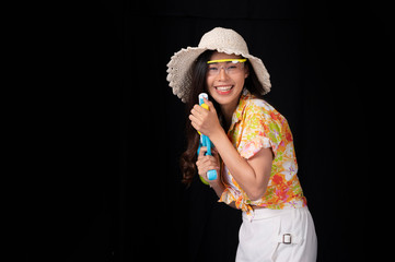 Portrait cheerful young asian woman with red glasses holding plastic water gun on balck background. Songkarn festival, Thailand. Thai New Year's Day. Isolated black  background.