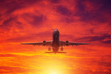 Fototapeta Na sufit - Airplane take off from the airport on the background of evening clouds and btight red sunset.
