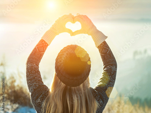 Happy traveler woman tourist stay on mountain top and making of love heart by hands in sunny frozen winter day.\
Health care, authenticity, sense of balance and calmness.