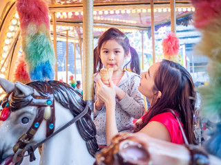 Wall Mural - happy asia mother and daughter have fun in amusement carnival park with farris wheel and carousel background