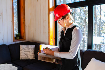 Wall Mural - caucasian woman inspector during pre-purchase inspection, she wearing a red hardhat and protective eyewear and using a clipboard, home interior review