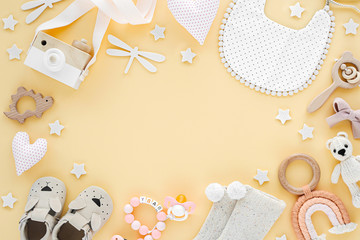 Toys, bib, socks, slippers for newborn on yellow background.  Frame made of  gender neutral baby stuff and accessories. Flat lay, top view