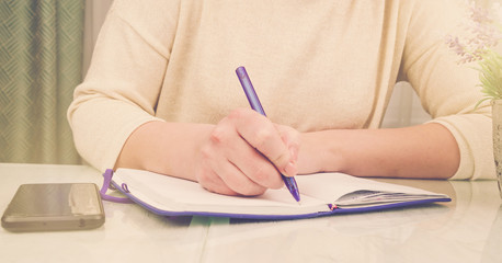 Wall Mural - woman in pullover writes in paper notebook with purple pen near lavender pot plant