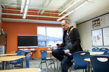 Male Junior High Teacher Using Smart Phone In Classroom