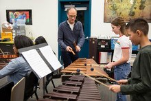 Junior High Teacher Guiding Students Playing Xylophones In Music Class
