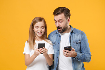 Wall Mural - Amazed bearded man in casual clothes with child baby girl. Father little kid daughter isolated on yellow background. Love family day parenthood childhood concept. Use mobile phone typing sms message.