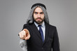 Strict bearded arabian muslim businessman in keffiyeh kafiya ring igal agal classic black suit isolated on gray background. Achievement career wealth business concept. Pointing index finger on camera.