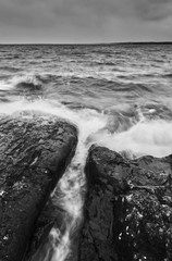 Wall Mural - Black and white photo waves rushing in over stones and rocks