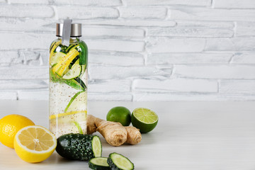 Wall Mural - Detox infused water with lemon, lime, ginger and cucumber in a glass sport bottle on white wooden background over brick wall.