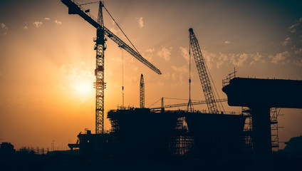 Silhouette of building at construction site with industrial crane in Dubai UAE at sunset sky background.