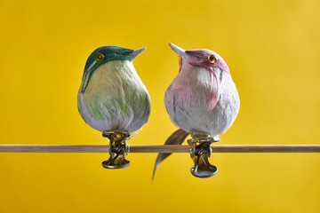 Fake birds with clips on a wooden stick. Christmas tree decoration birds against a yellow background. Communication or vintage concept.