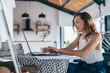 © undrey - Woman using laptop while sitting at home. Young woman sitting in kitchen and working on laptop.
