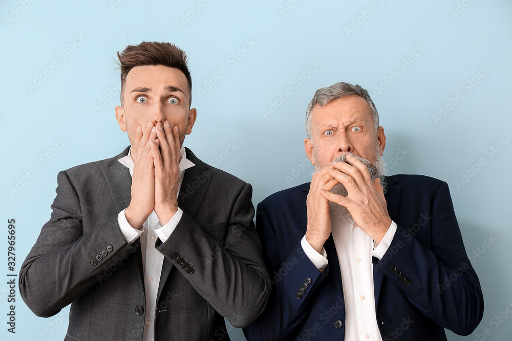 Afraid senior man and his adult son on color background