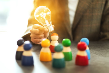 Wall Mural - Closeup image of a woman holding and putting a light bulb over one of a different colors wooden people toy for business concept